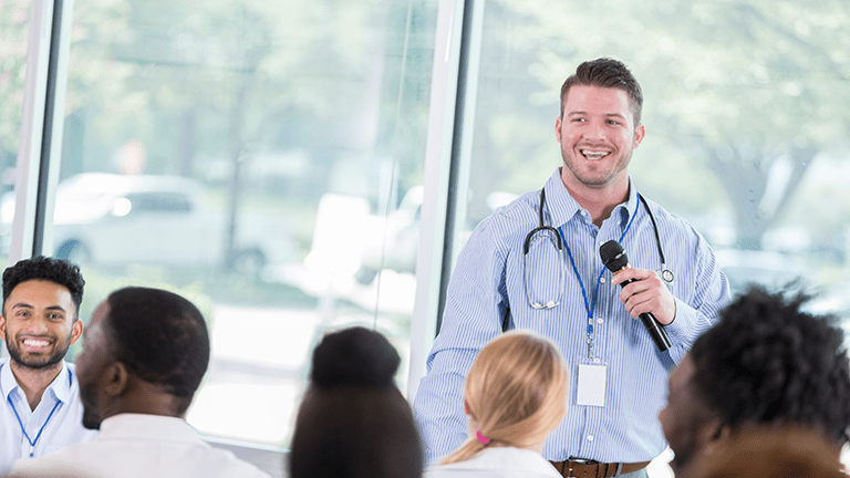 Young male healthcare student smiles as he speaks to a group of classmates in a school.