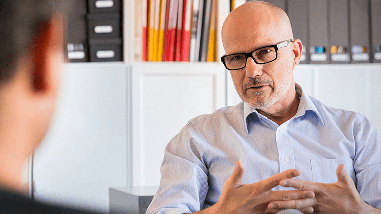 Mature male counsellor interacts with a male client during a one-to-one therapy session.