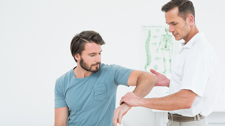 Male physical therapist examining a patient's arm.