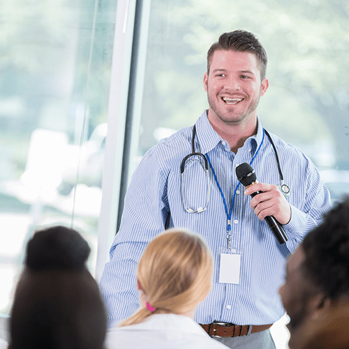 Young male healthcare student smiles as he speaks to a group of classmates in a school.