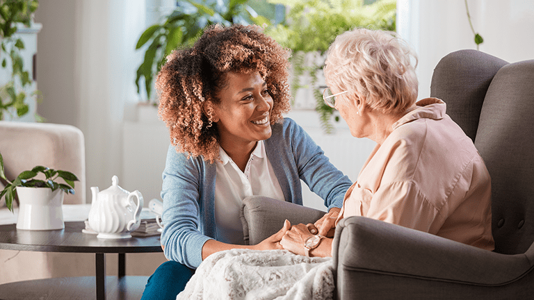 Female caregiver talking with senior woman, sitting and listening to her carefully.