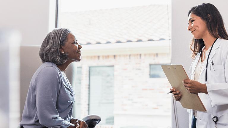 A caring female physician assistant smiles with compassion while talking with a senior female patient during a medical exam.