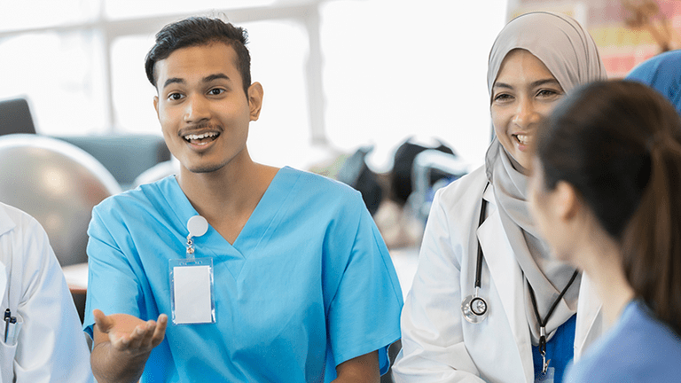 An excited young male healthcare student sits in a circle with classmates and gestures as he speaks to them.