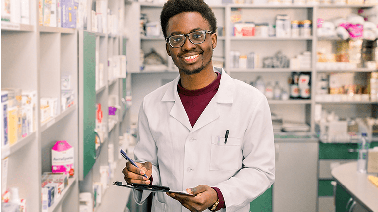Male Pharmacist smiles at camera while holding clipboard.