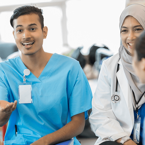 An excited young male healthcare student sits in a circle with classmates and gestures as he speaks to them.